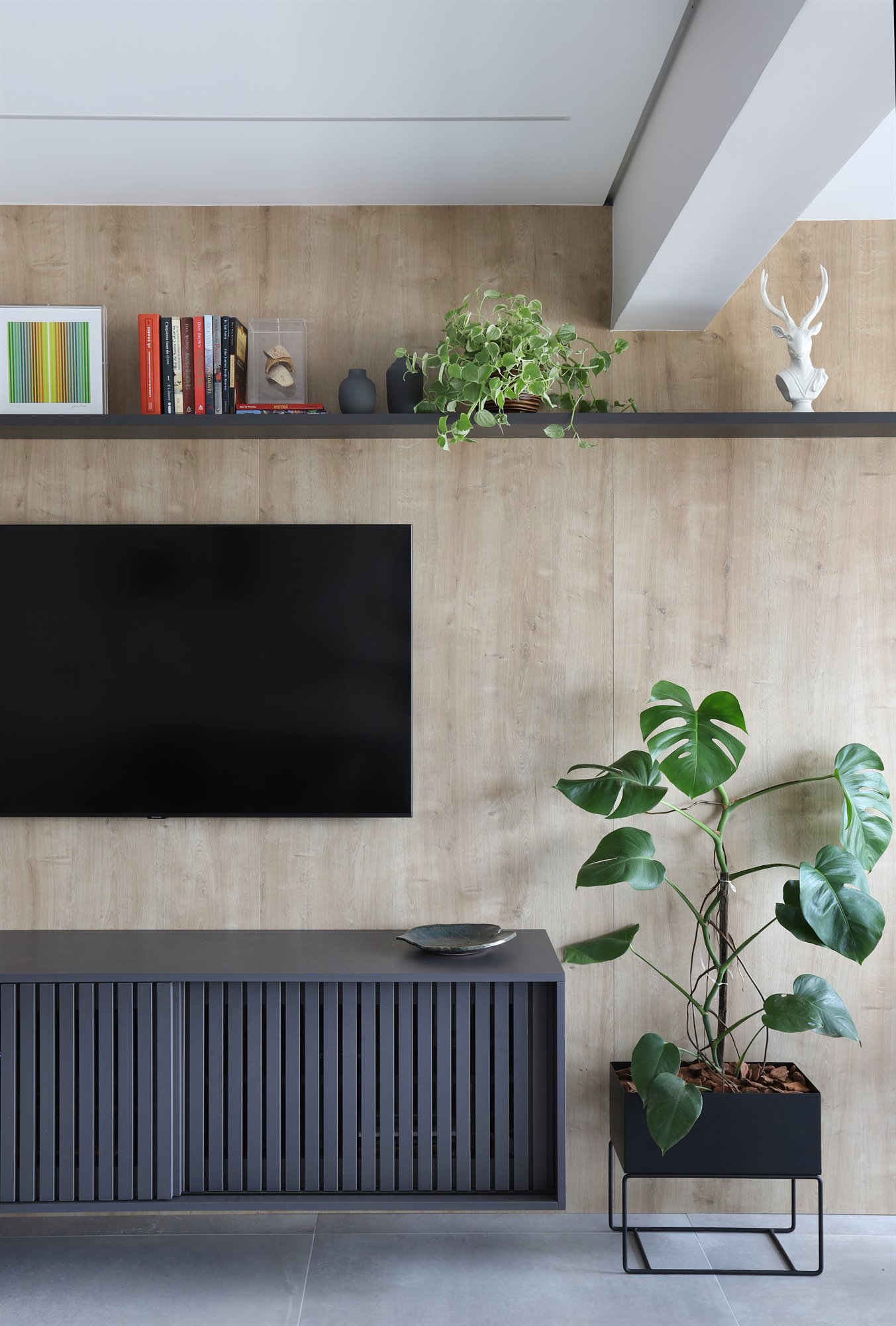 Projeto Lapa: Sala de estar com painel amadeirado, rack ripado escuro e plantas.