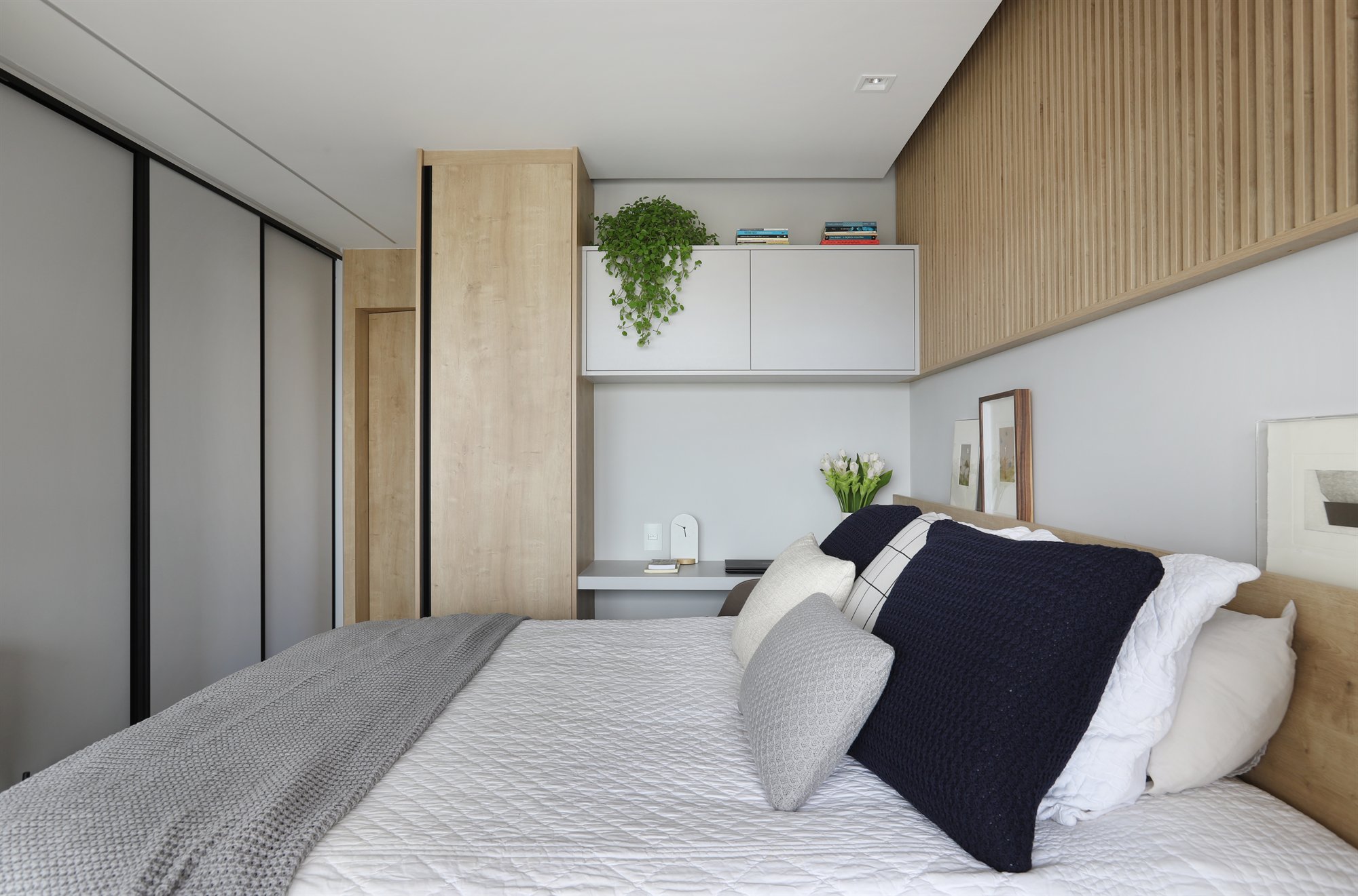 Projeto Lapa: Dormitório com cama de casal, armários e painel ripado de madeira.