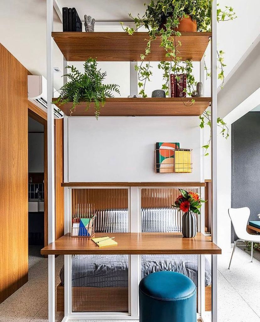 Projeto Liberdade: Divisória de marcenaria com estantes, plantas e bancada de trabalho.