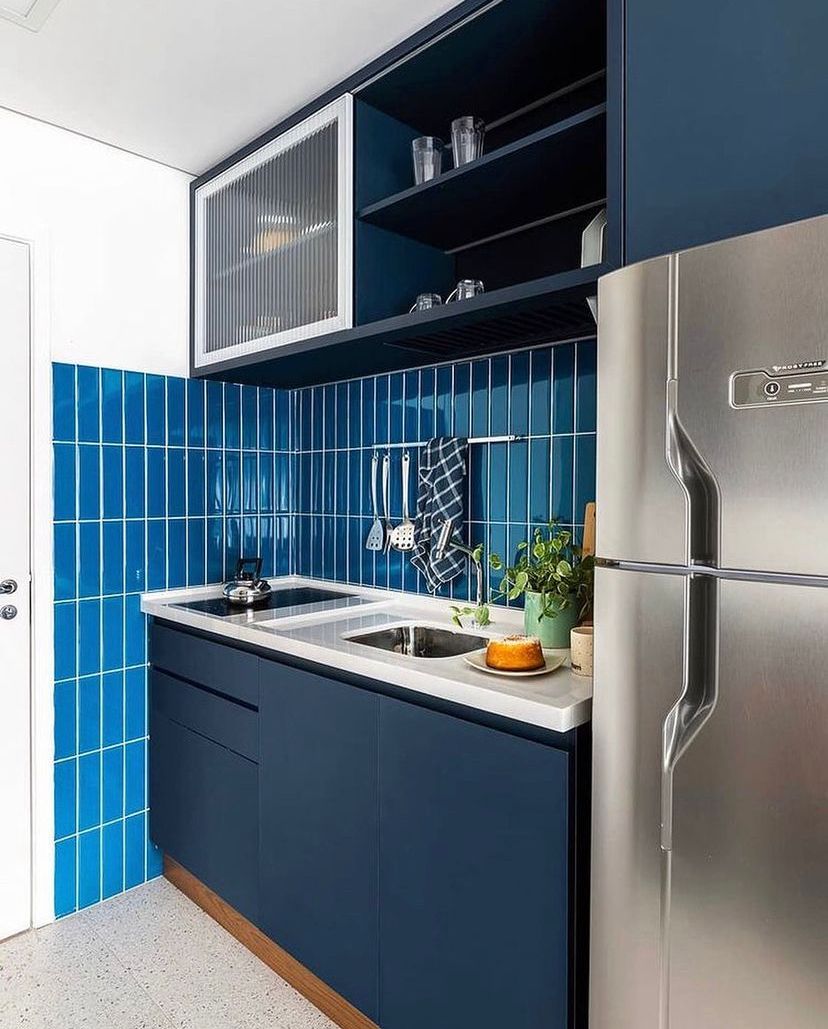 Projeto Liberdade: Cozinha compacta com armários azul-marinho, azulejos azuis e eletrodomésticos em inox.