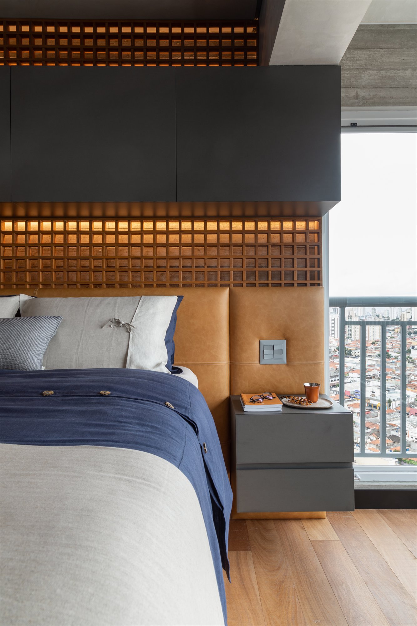 Projeto Mooca: Cama com cabeceira estofada caramelo e treliça de madeira, junto à varanda.