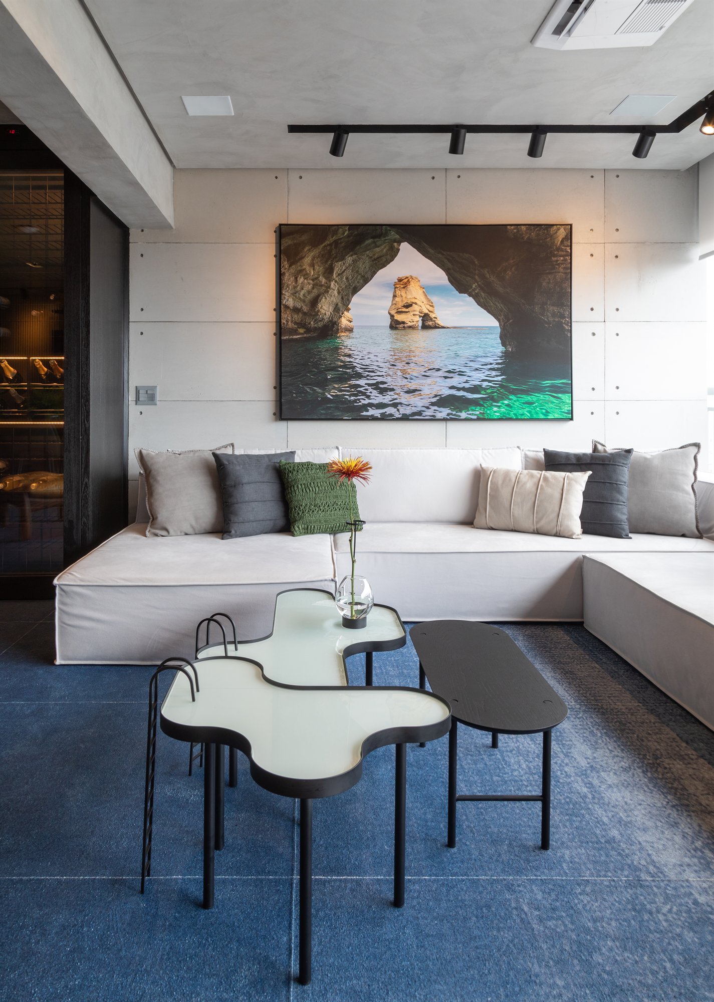 Projeto Mooca: Outra vista da sala com sofá branco, mesas orgânicas e tapete azul.
