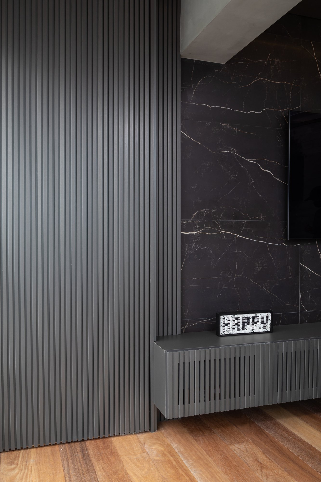 Projeto Mooca: Painel ripado cinza com TV e rack suspenso diante do revestimento escuro.