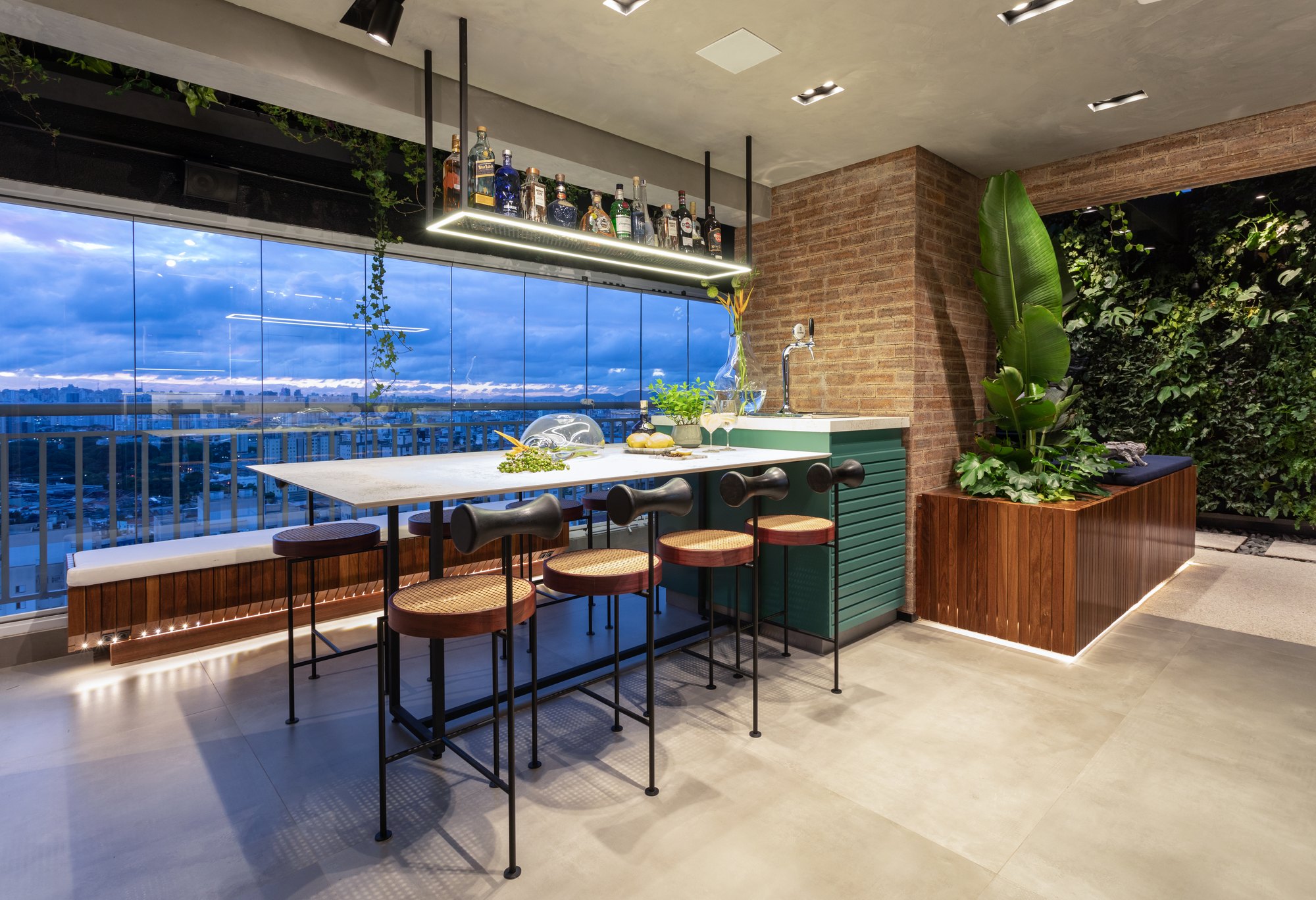 Projeto Mooca: Varanda gourmet com bancada e banquetas diante da piscina e do jardim vertical.