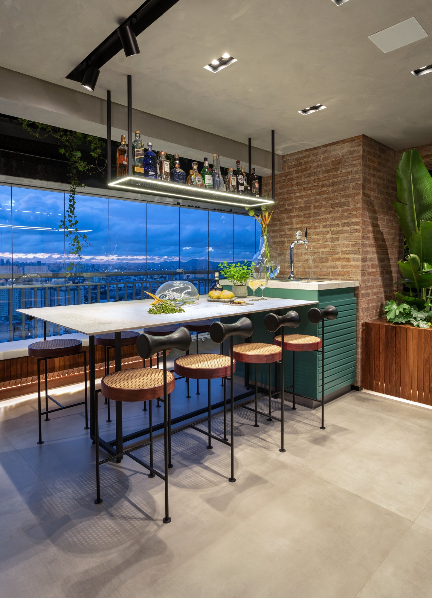 Projeto Mooca: Bancada gourmet com banquetas, tijolos aparentes e vista da cidade ao entardecer.