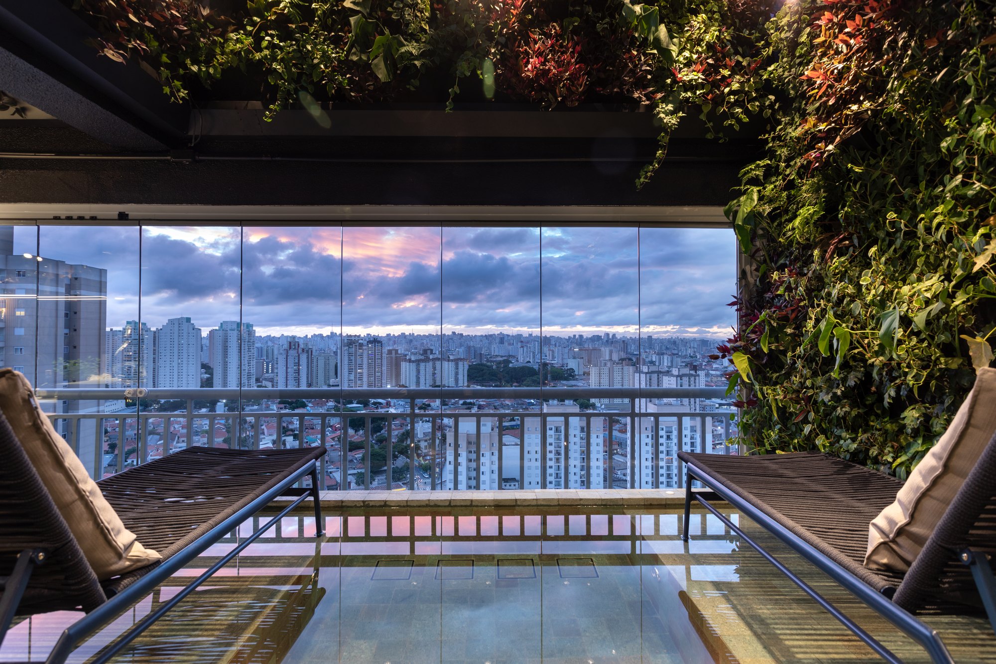 Projeto Mooca: Piscina com espreguiçadeiras, fechamento de vidro e vista para a cidade.