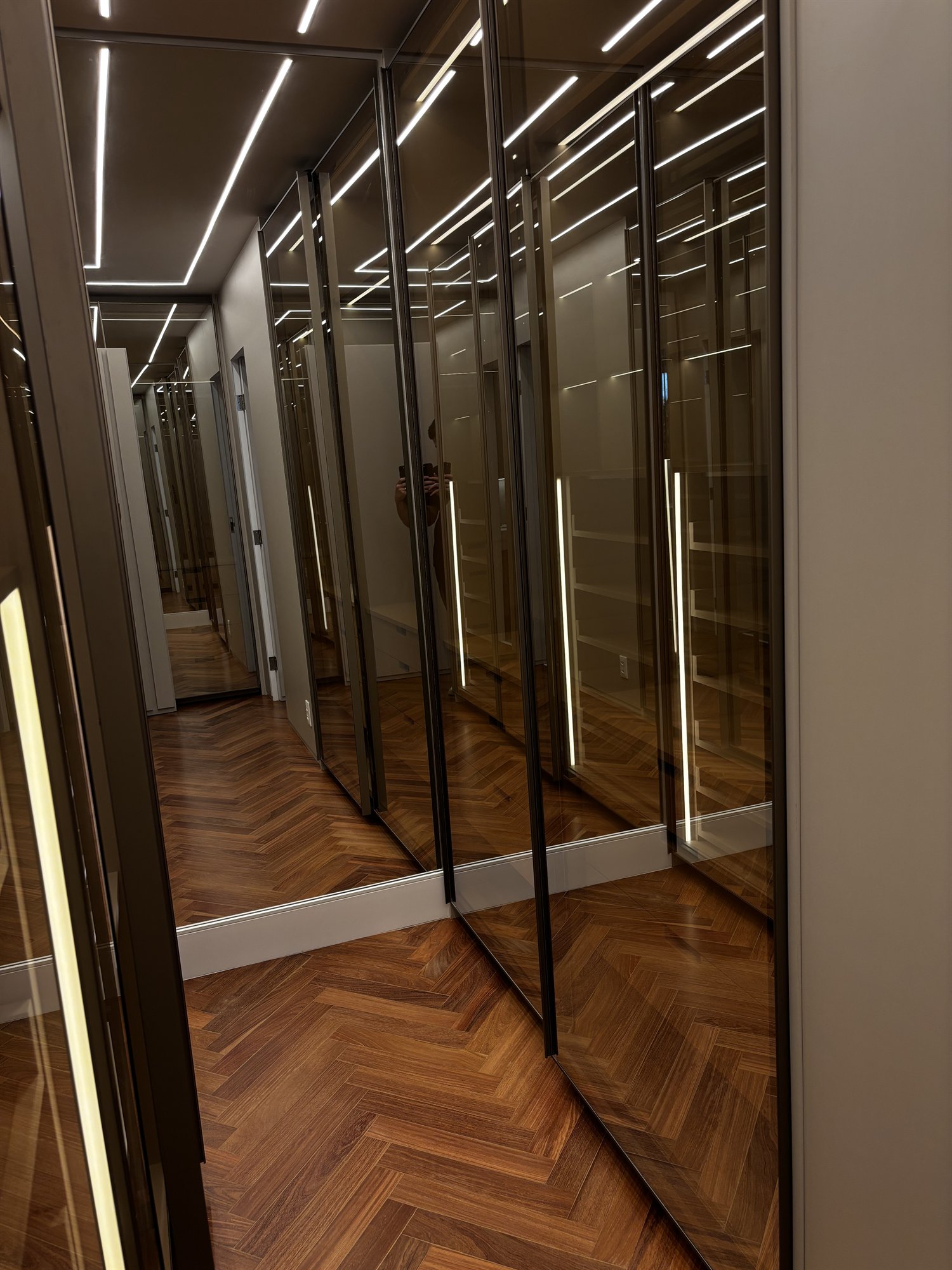 Projeto Perdizes: Closet com portas de vidro, perfis pretos e iluminação embutida.