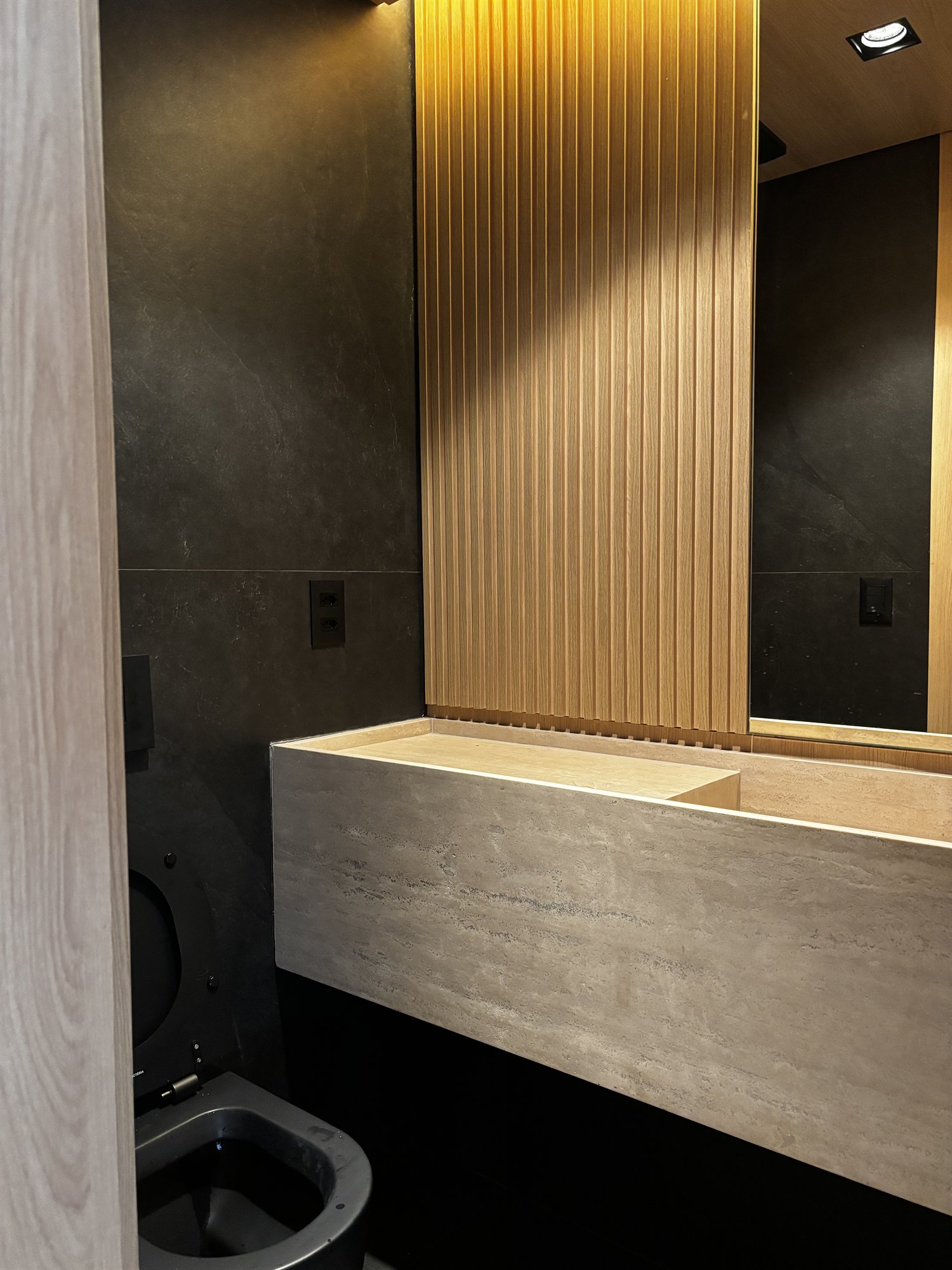 Projeto Perdizes: Lavabo com bancada de pedra, painel ripado de madeira e iluminação indireta.