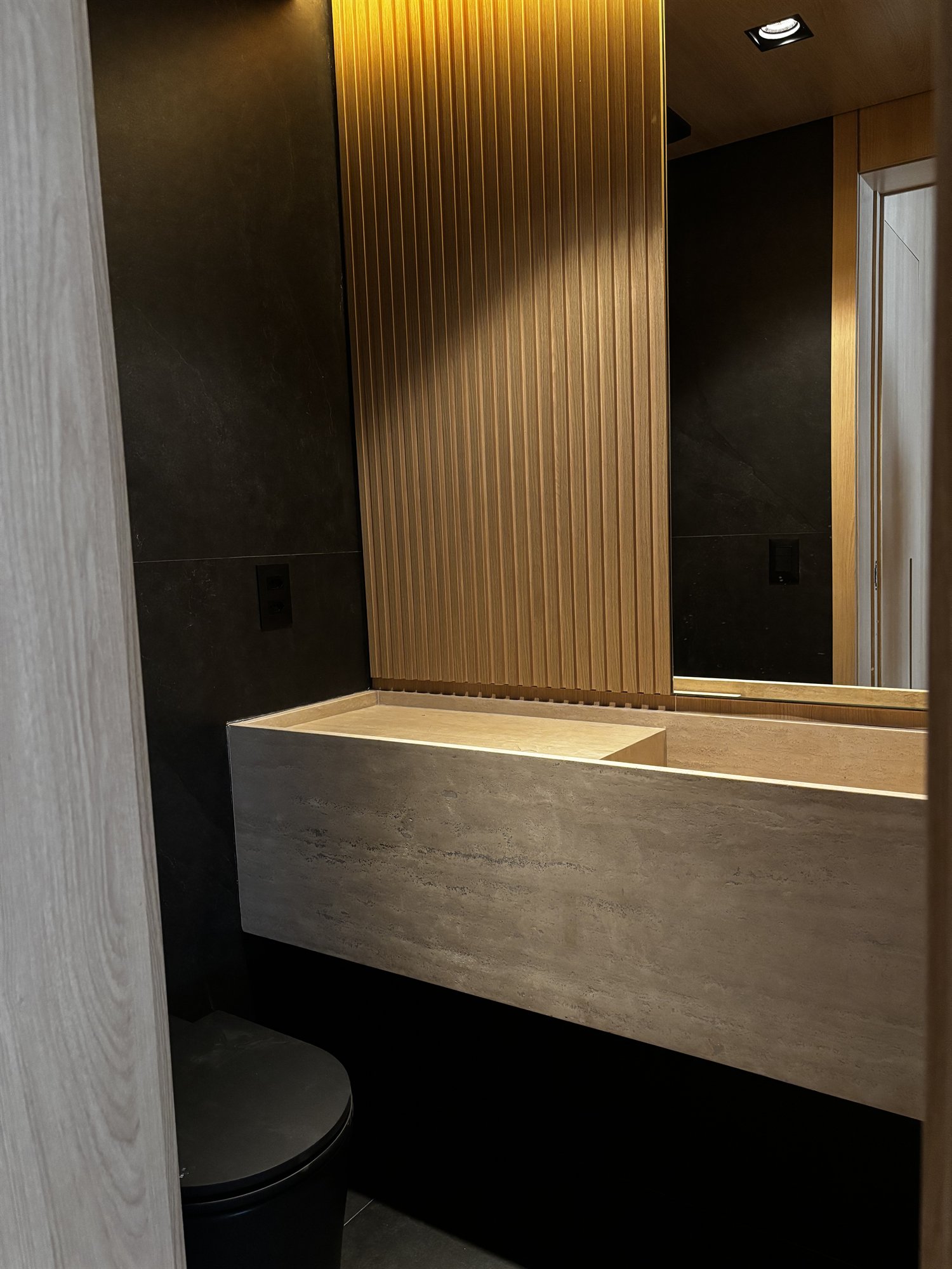 Projeto Perdizes: Lavabo com cuba esculpida, marcenaria ripada de madeira e espelho iluminado.