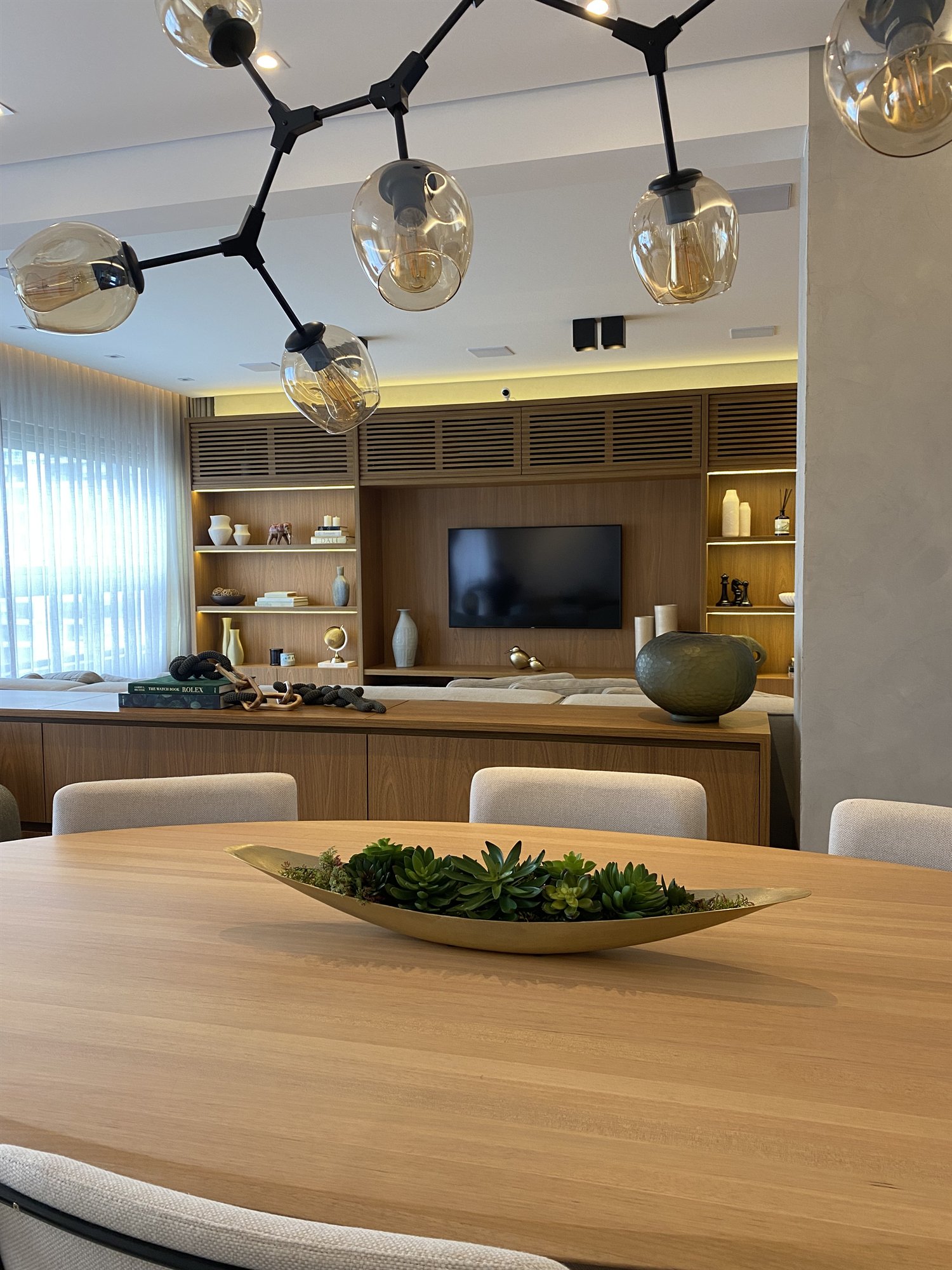 Projeto Itaim Bibi 2024: Sala de jantar com mesa de madeira, luminária escultural e marcenaria ao fundo.