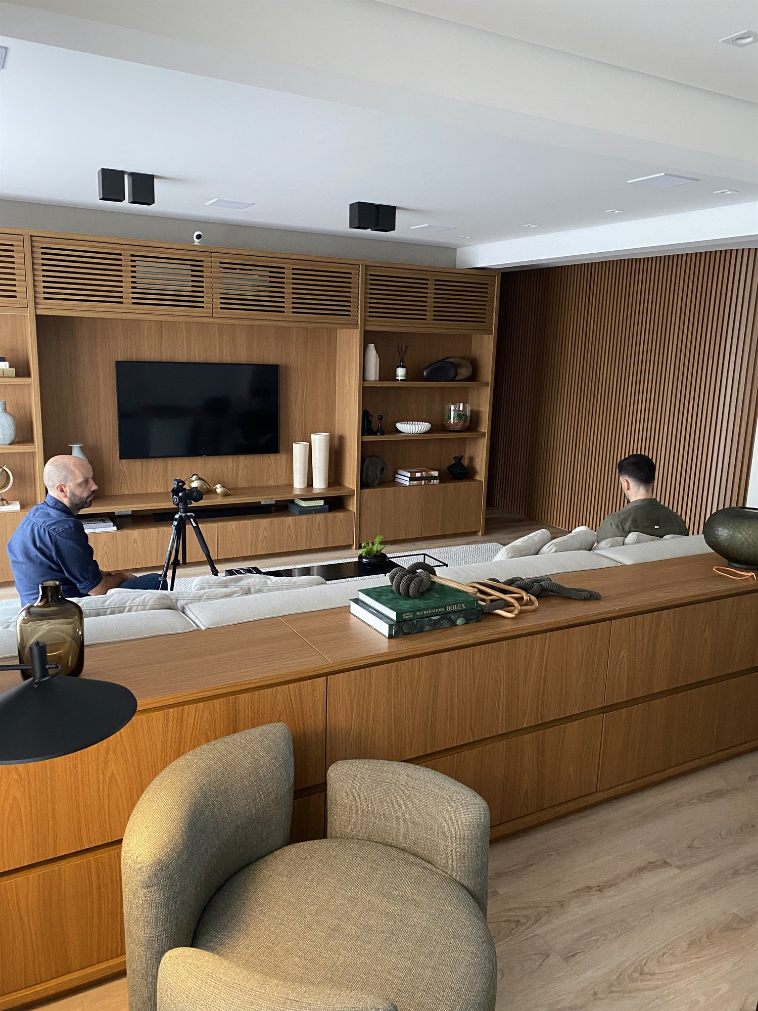 Projeto Itaim Bibi 2024: Vista ampla da sala com sofá, painel de TV e marcenaria de madeira.