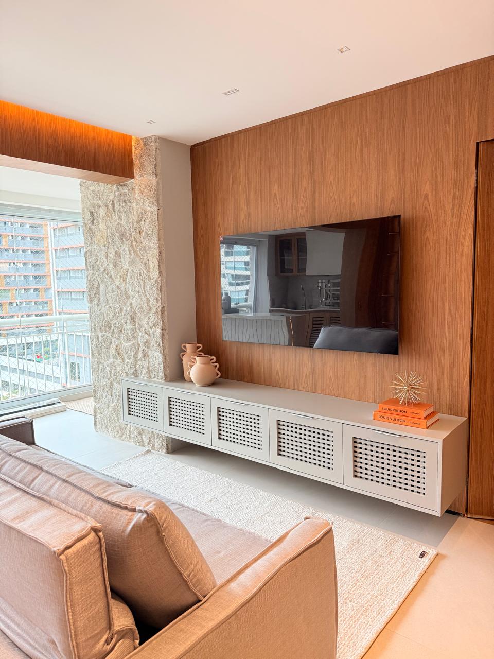 Projeto Santo Amaro: Sala com painel de madeira, pedra natural e rack planejado.