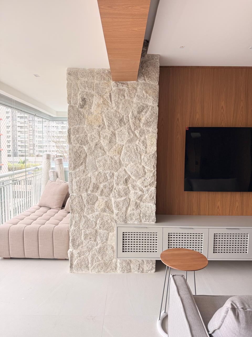 Projeto Santo Amaro: Sala com painel de TV, pedra natural e marcenaria.