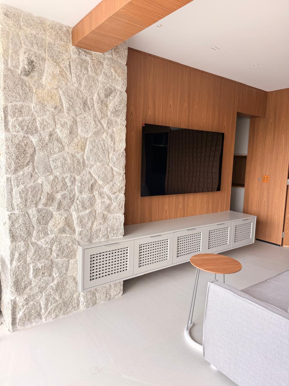 Projeto Santo Amaro: Sala com painel de TV e revestimento de pedra natural.