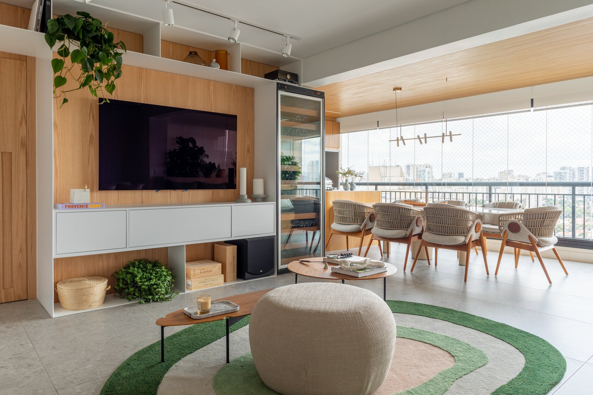 Projeto Vila Olimpia: Sala integrada com painel de madeira, TV, adega e sala de jantar na varanda.