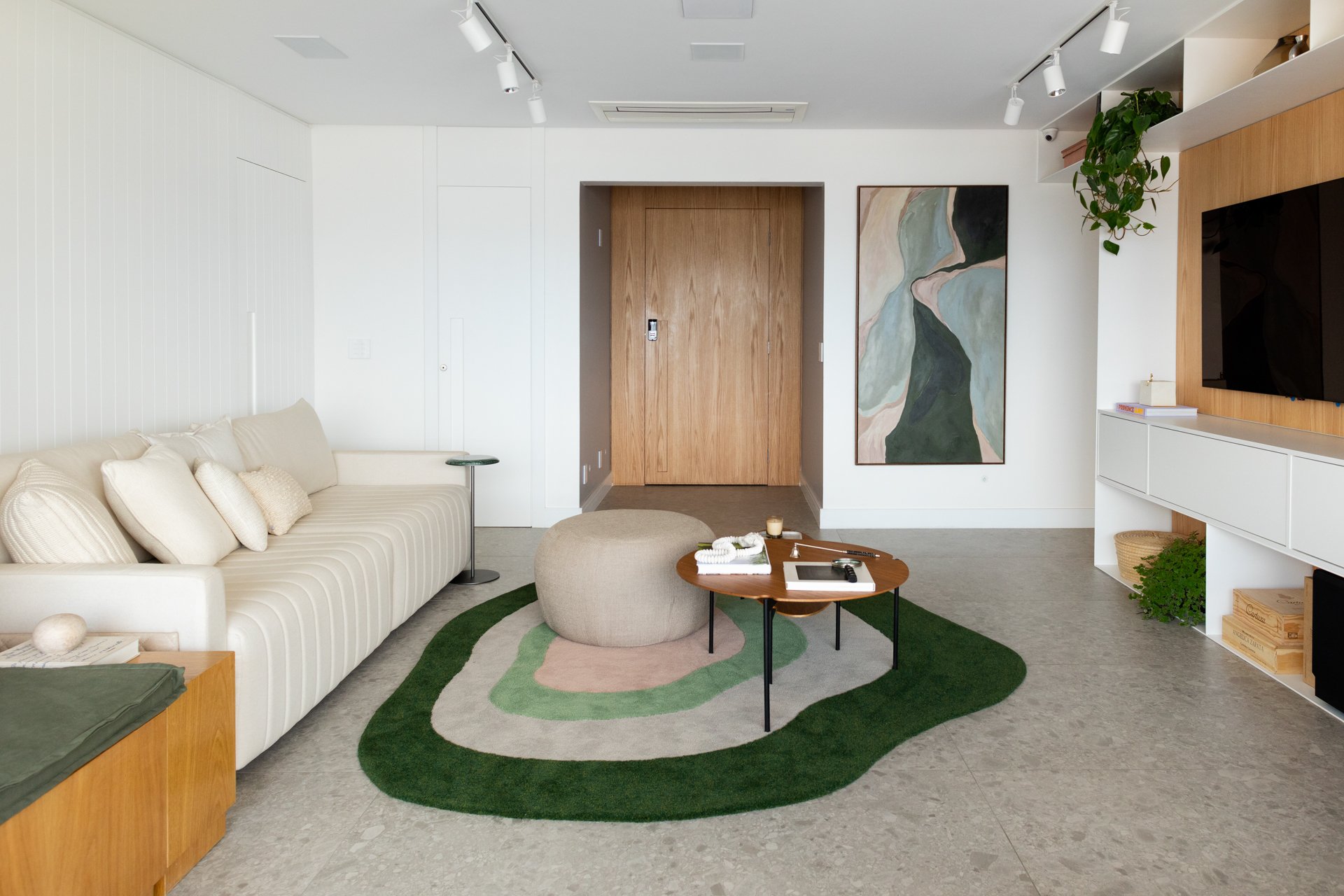 Projeto Vila Olimpia: Sala com sofá claro, tapete verde e porta de madeira.