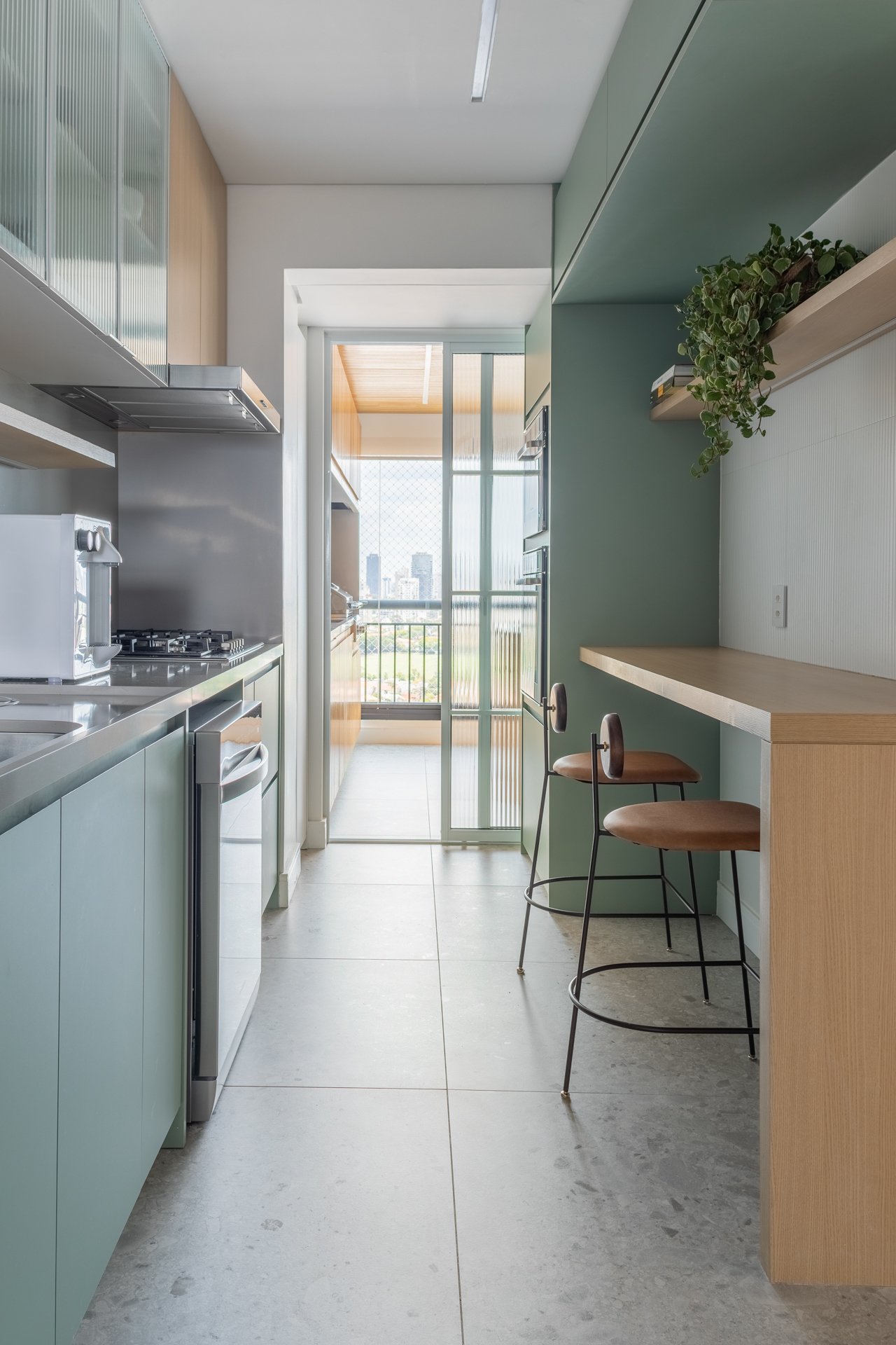 Projeto Vila Olimpia: Cozinha estreita com marcenaria verde, bancada e bancos.