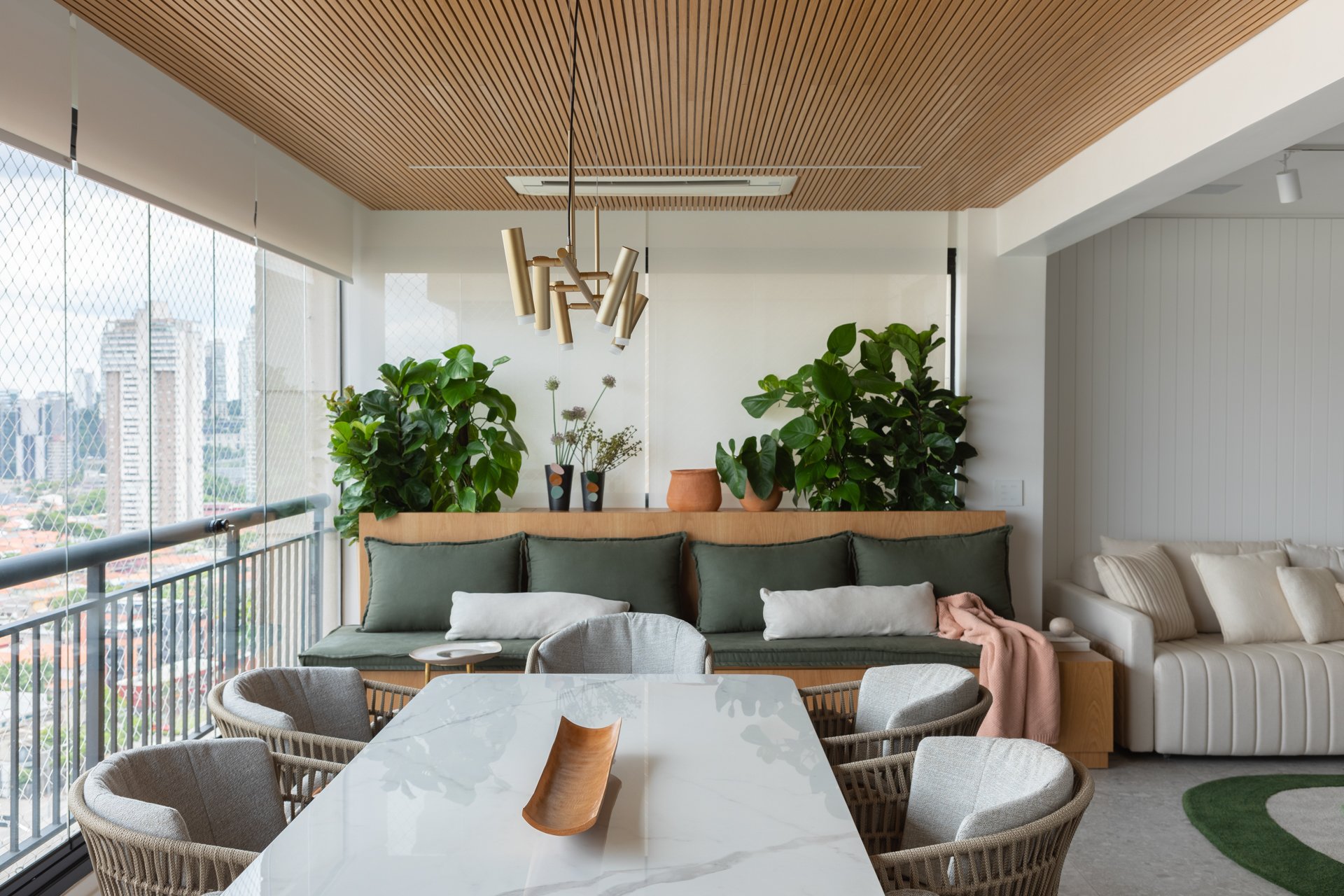 Projeto Vila Olimpia: Varanda com mesa de jantar, banco verde e plantas.