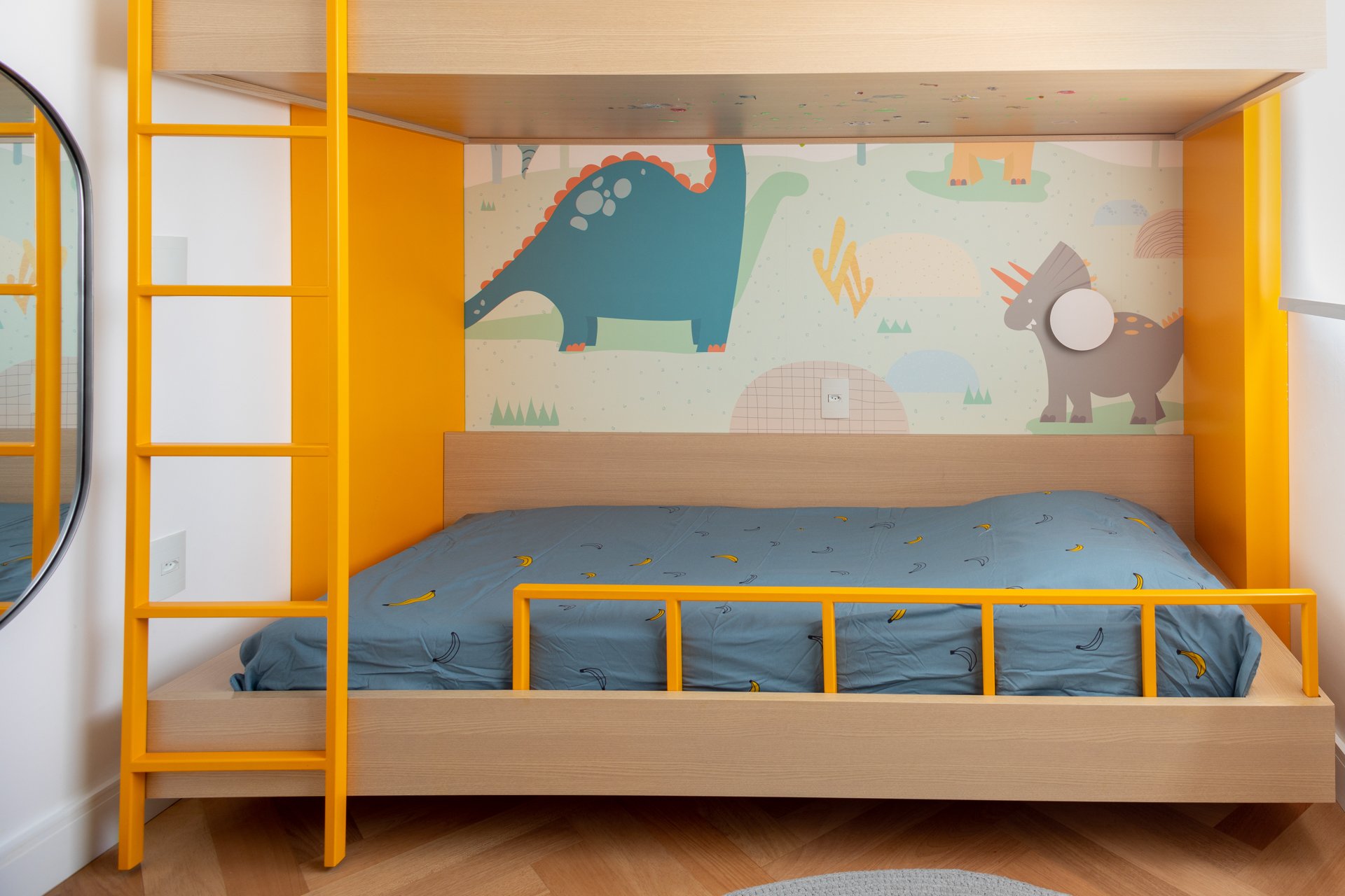 Projeto Vila Olimpia: Cama infantil integrada a estrutura de madeira e escada amarela, com mural de dinossauros.