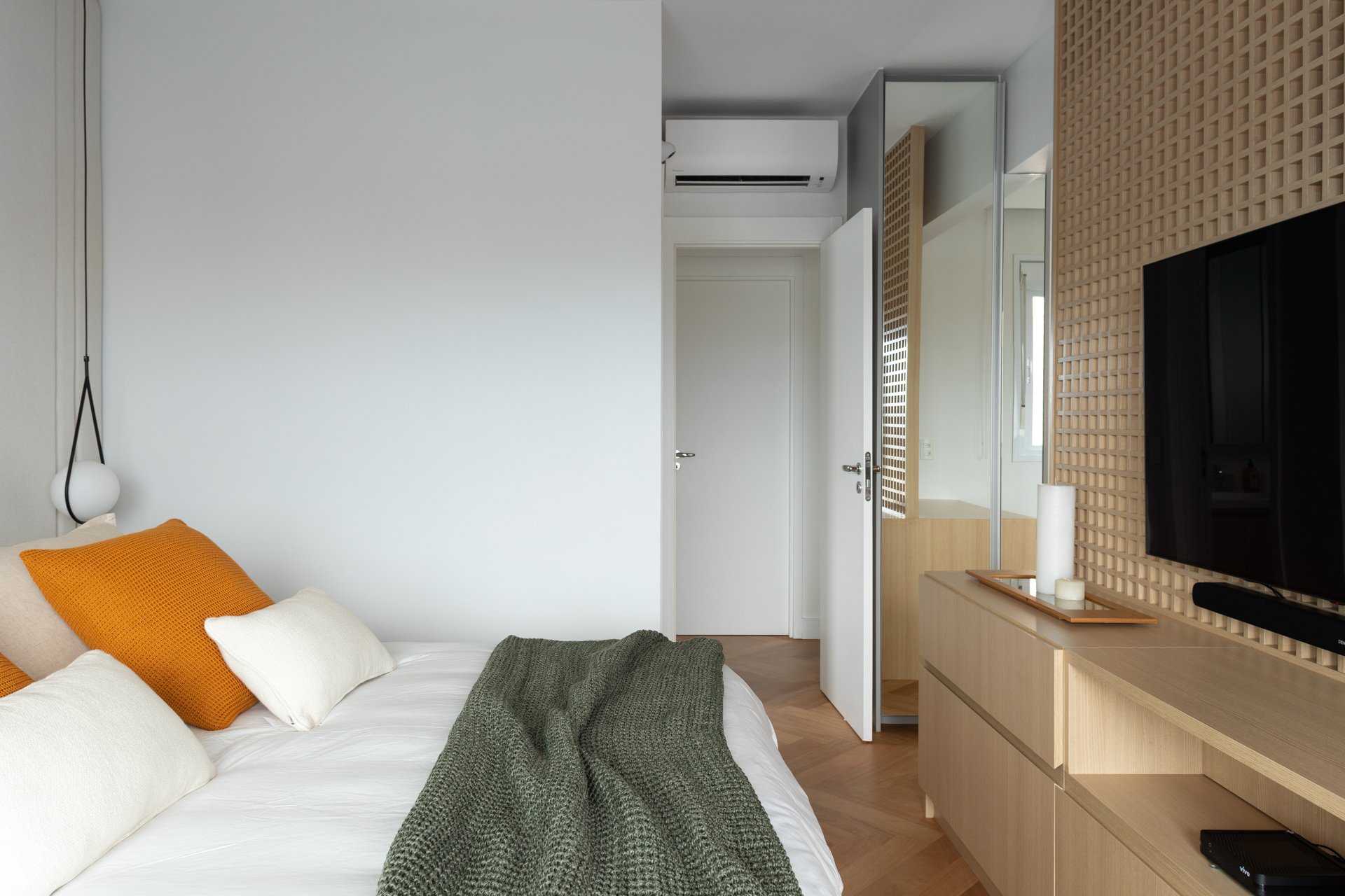 Projeto Vila Olimpia: Quarto com cama, painel de televisão em treliça de madeira e armário espelhado.